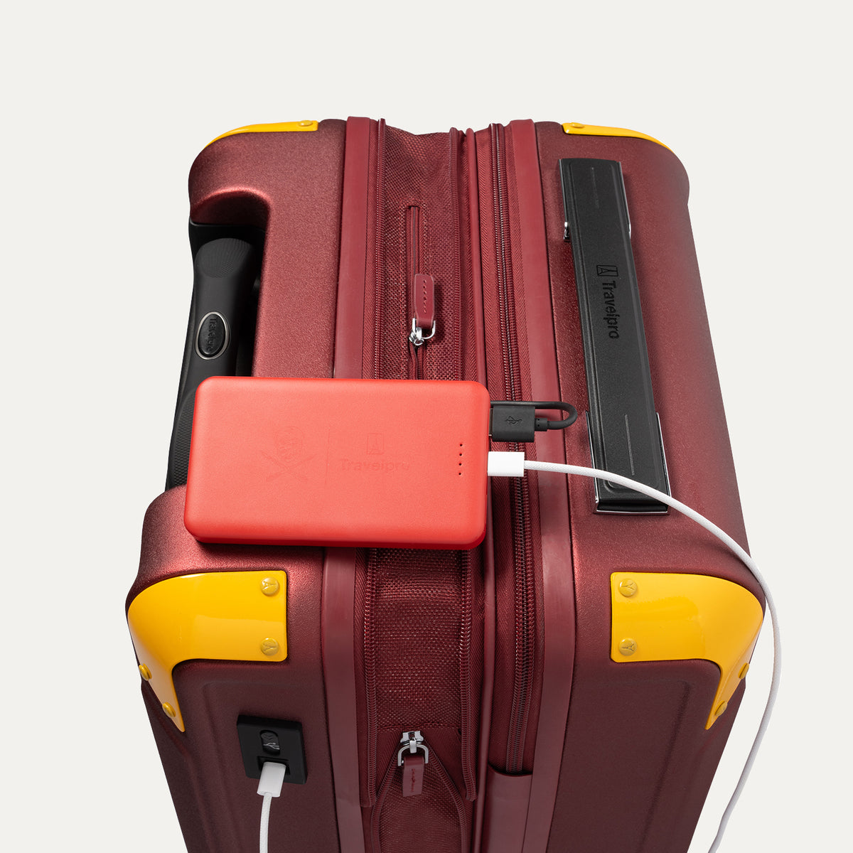 Travelpro x Surgeon Spinner in Daring Red with yellow accents, shown with matching red power bank connected to exterior USB port.
