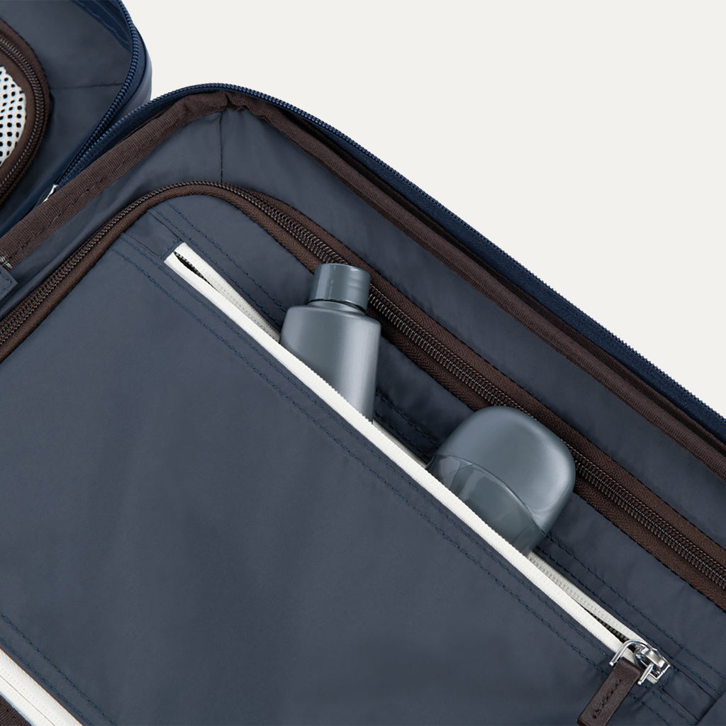 Interior view of Travelpro Platinum Elite Compact Carry-On Hardside Spinner in True Navy, showing zippered pocket with visible travel-size toiletries.


