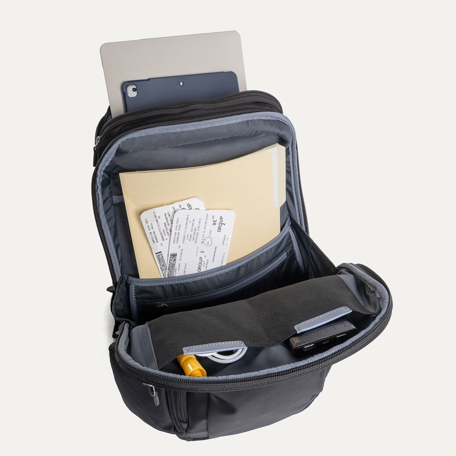 Black backpack with compartments containing a tablet, notebook, and documents on a white background