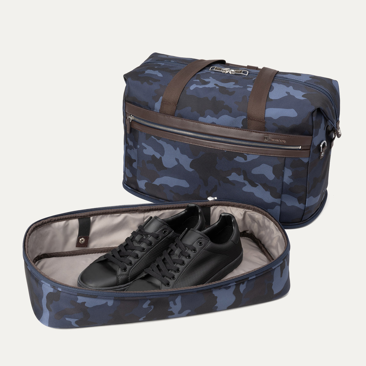 Slanted front view of Travelpro Platinum Elite Drop-Bottom Weekender in Navy Camouflage with detached drop-bottom compartment holding shoes.
