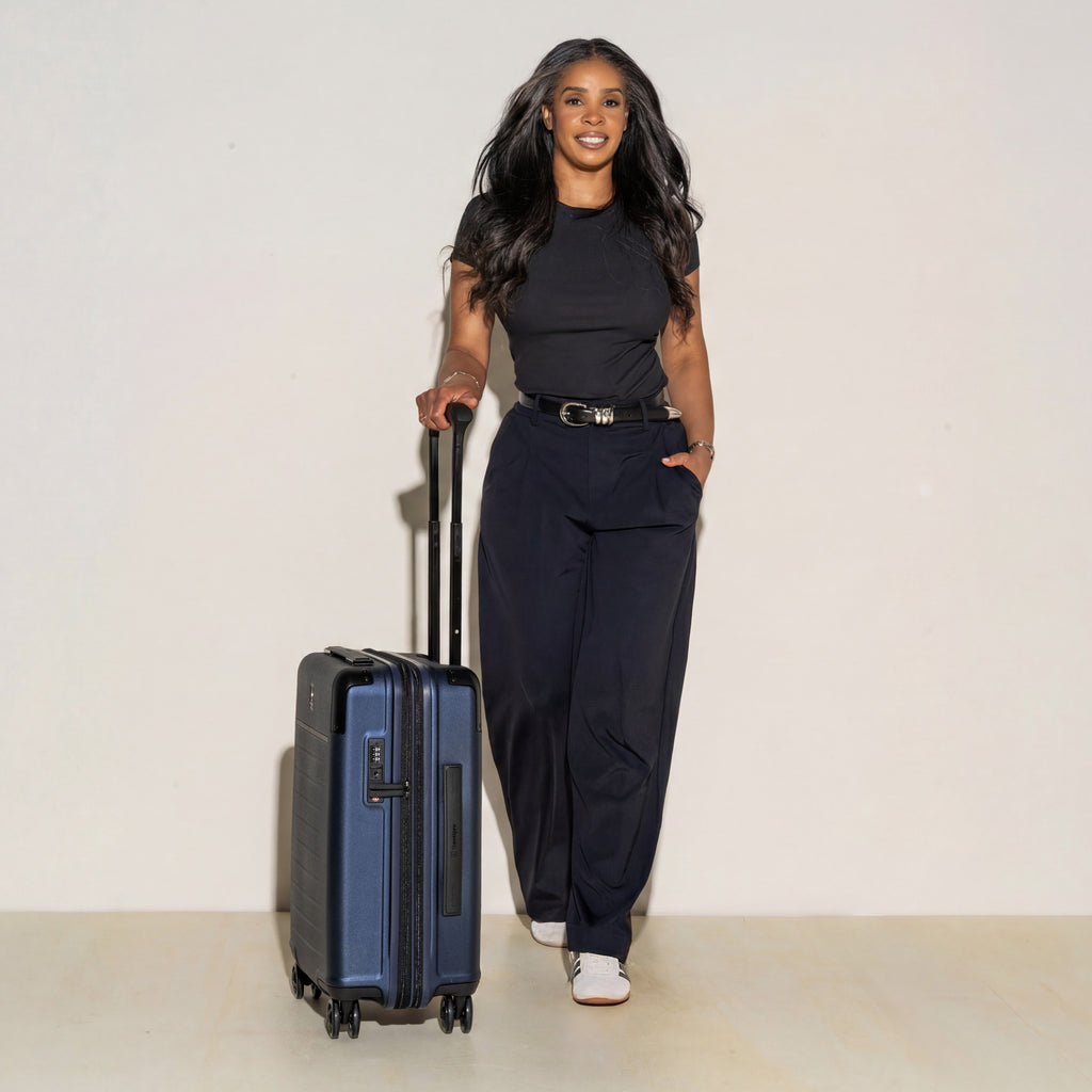 Woman standing next to a blue suitcase against a plain background