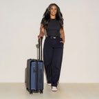 Woman standing next to a blue suitcase against a plain background