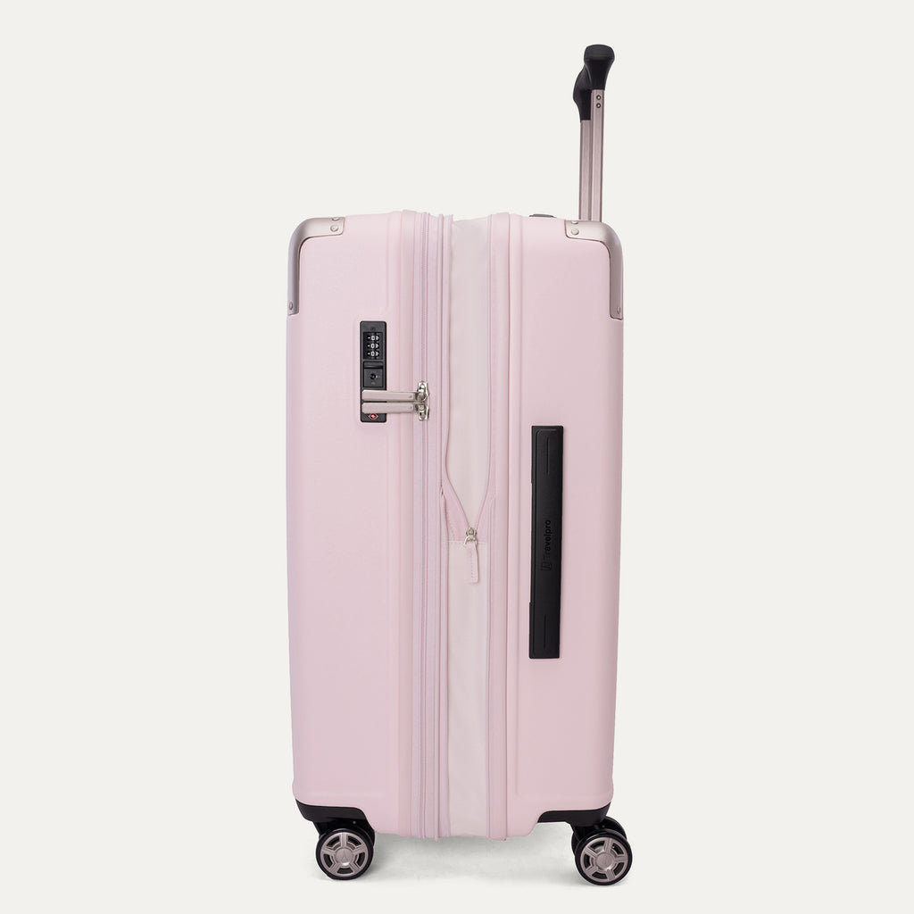 Side view of the Travelpro Platinum Elite Medium Check-In Hardside Spinner in Powder Pink, shown in its expanded position to highlight the 2-inch zippered expansion feature, side carry handle, and smooth-rolling wheels against a clean off-white background.