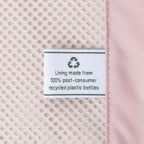 Close-up detail of the ECOFAB™ lining inside the Travelpro Platinum Elite Medium Check-In Hardside Spinner, showing a white fabric label that reads "Lining made from 100% post-consumer recycled plastic bottles" with a green recycling symbol against the pink mesh interior.
