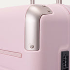 Close-up of the Travelpro Platinum Elite Medium Check-In Hardside Spinner in Powder Pink, featuring protective polished aluminum corner armor, an integrated TSA-approved combination lock, and smooth side zipper trim against a clean off-white background.
