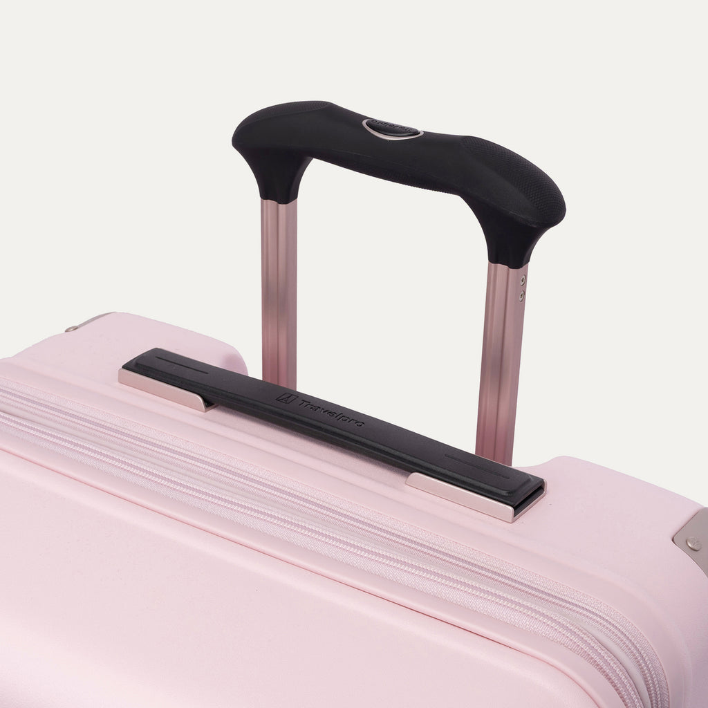 Close-up of the Travelpro Platinum Elite Medium Check-In Hardside Spinner in Powder Pink, highlighting the multi-stop PowerScope Lite telescoping handle, the rubberized Contour Grip, and the top carry handle against a clean off-white background.