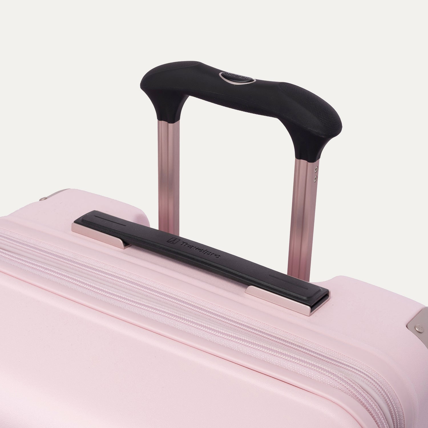 Close-up of the Travelpro Platinum Elite Medium Check-In Hardside Spinner in Powder Pink, highlighting the multi-stop PowerScope Lite telescoping handle, the rubberized Contour Grip, and the top carry handle against a clean off-white background.