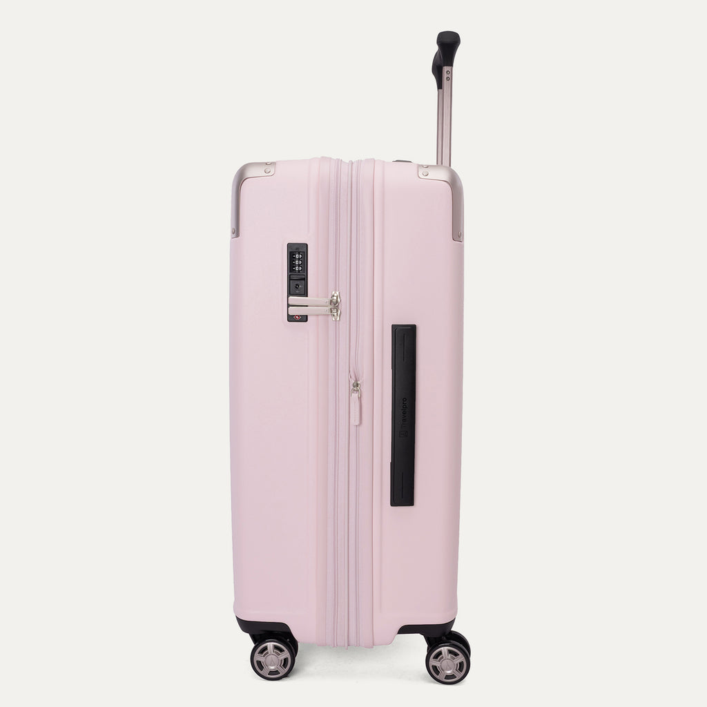 Side view of the Travelpro Platinum Elite Medium Check-In Hardside Spinner in Powder Pink, featuring a durable polycarbonate shell with polished aluminum corner armor, an extended telescopic handle, and multi-directional wheels against a clean off-white background.