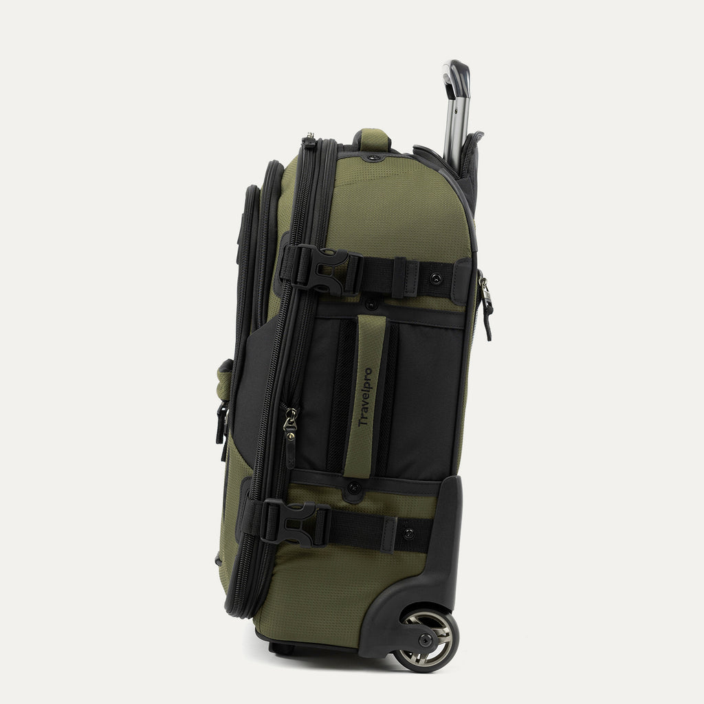 side view of the olive black bold by travelpro carry-on expandable rollaboard suitcase standing vertically, showing its durable army green fabric accent panels, padded side carry handle, exterior compression straps with buckles, a high-performance corner-mounted wheel, and the extended telescoping handle.
