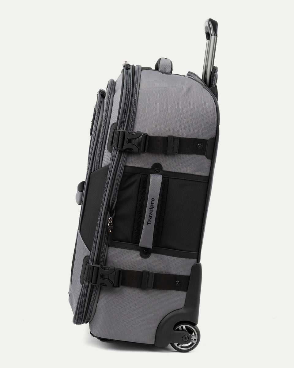 side view of the gray black bold by travelpro medium check-in expandable rollaboard suitcase standing vertically, showing its durable gray fabric accent panels, side carry handle, exterior compression straps with buckles, and the extended telescoping handle.