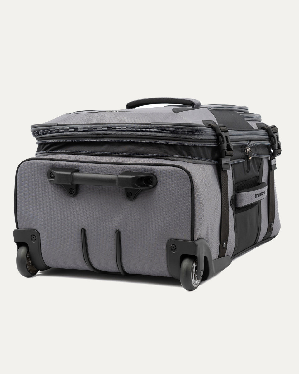 low-angle rear view of the gray black bold by travelpro medium check-in expandable rollaboard suitcase resting horizontally, showcasing its two high-performance ball-bearing wheels, heavy-duty skid guards, and the molded housing around the retracted telescoping handle.