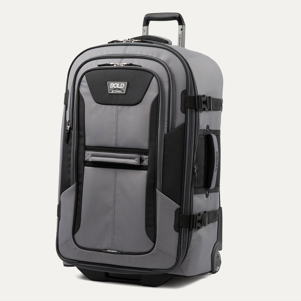 upright front three-quarter view of the gray black bold by travelpro large check-in expandable rollaboard suitcase standing vertically, showcasing its rugged black and gray polyester exterior, dual front zippered pockets, and extended telescoping aircraft-grade handle.