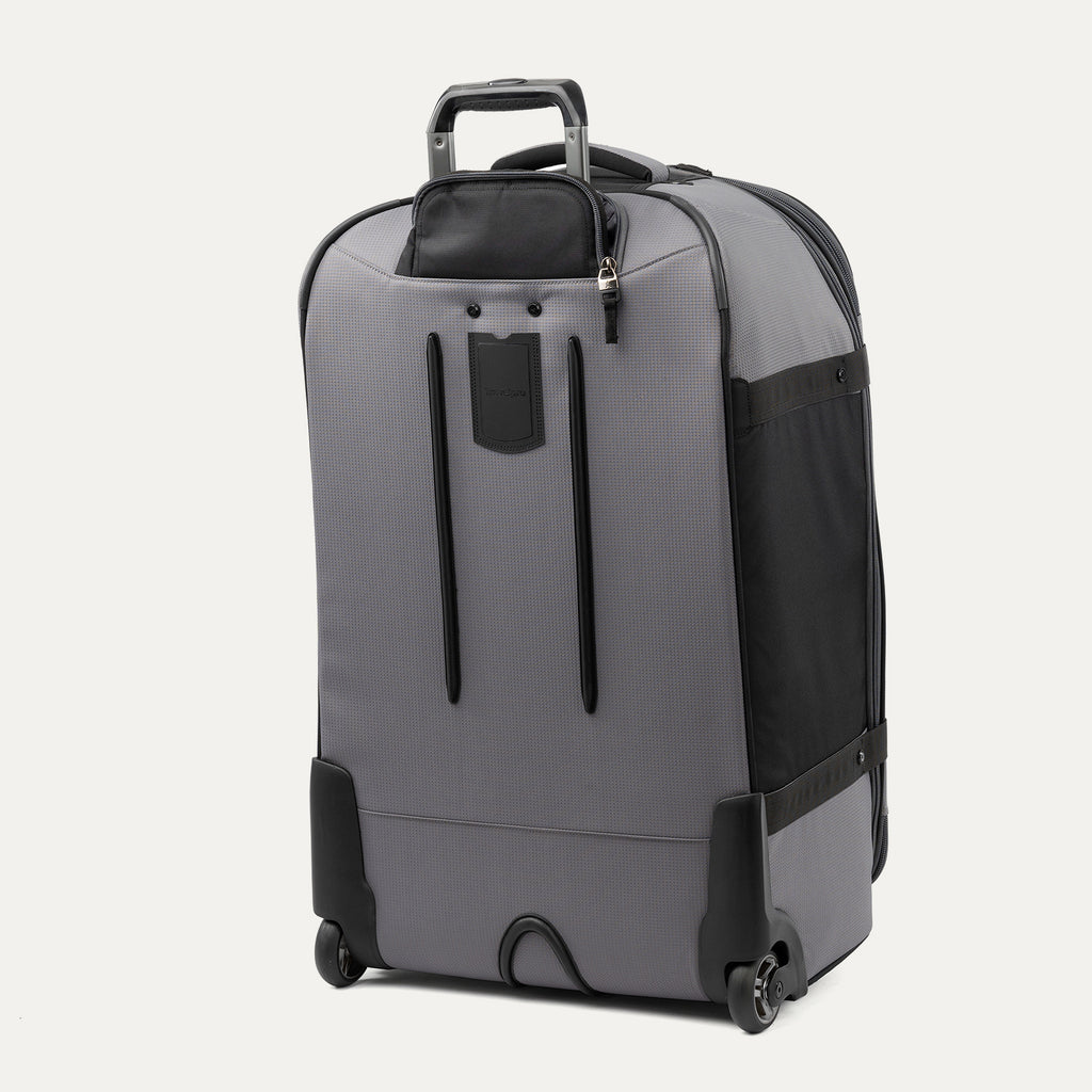 rear three-quarter view of the gray black bold by travelpro large check-in expandable rollaboard suitcase standing vertically, showing its protective skid guards, molded corner guards, reinforced wheel housings, two high-performance ball-bearing wheels, and extended telescoping handle.
