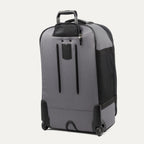 rear three-quarter view of the gray black bold by travelpro large check-in expandable rollaboard suitcase standing vertically, showing its protective skid guards, molded corner guards, reinforced wheel housings, two high-performance ball-bearing wheels, and extended telescoping handle.