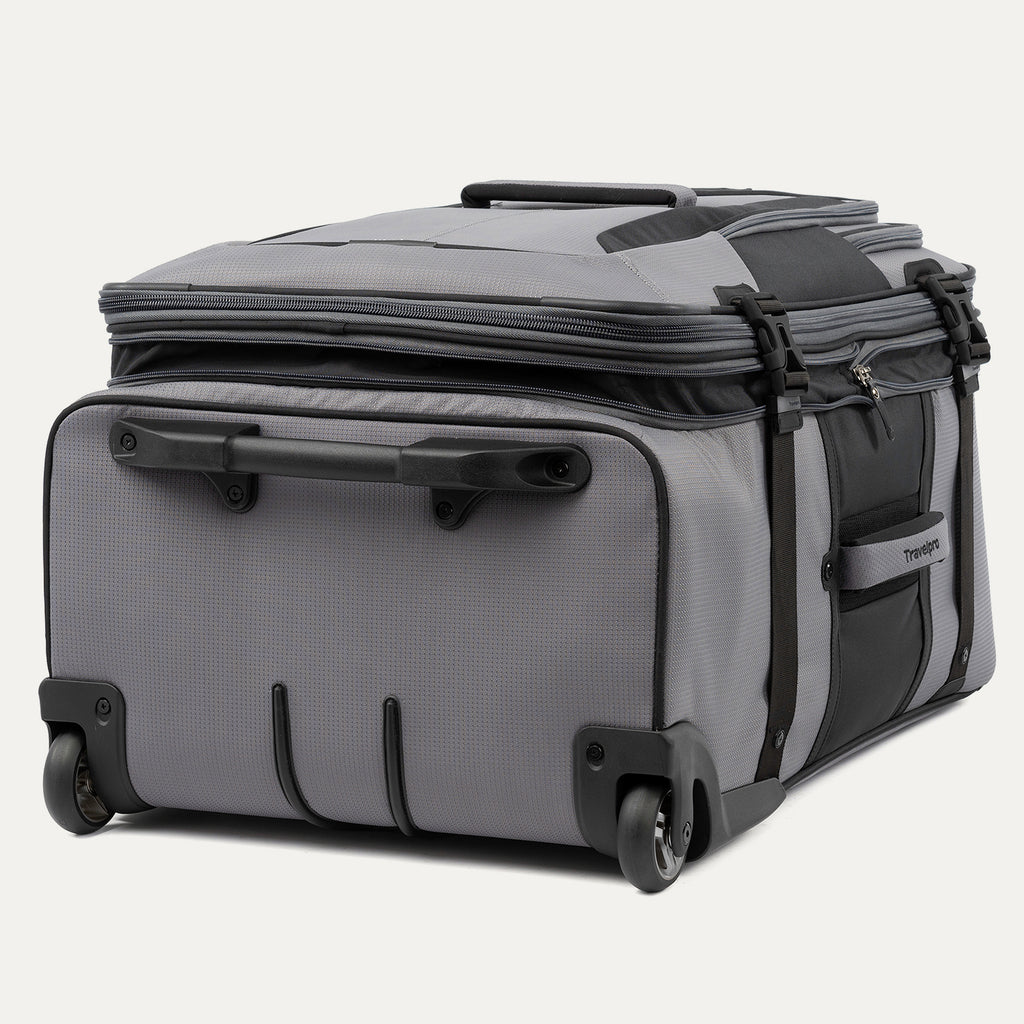 low-angle rear view of the gray black bold by travelpro large check-in expandable rollaboard suitcase resting horizontally, showcasing its two high-performance ball-bearing wheels, heavy-duty skid guards, and the molded housing around the retracted telescoping handle.