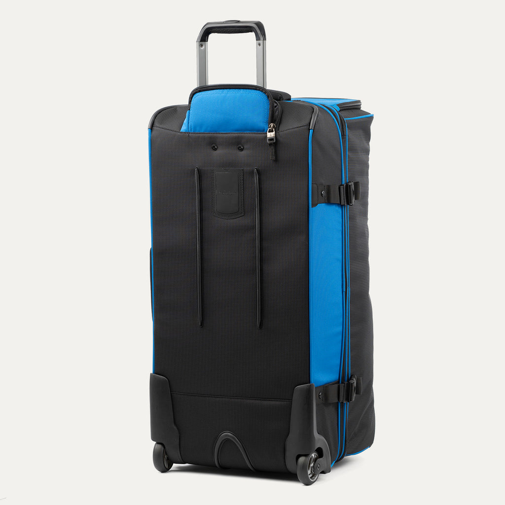 rear view of the blue black bold by travelpro large check-in drop-bottom rolling duffel bag standing vertically, showing its protective skid guards, reinforced wheel housings, two high-performance ball-bearing wheels, and extended telescoping handle.
