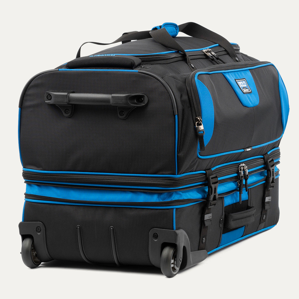 low-angle rear view of the blue black bold by travelpro large check-in drop-bottom rolling duffel bag resting horizontally, showcasing its two high-performance wheels, heavy-duty bottom skid guards, and the retracted telescoping handle base.