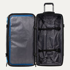 interior view of the open blue black bold by travelpro large check-in drop-bottom rolling duffel bag showing the spacious main compartment with two adjustable tie-down straps and a large zippered mesh pocket on the inside lid.