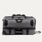 side view of the gray black bold by travelpro large check-in drop-bottom rolling duffel bag resting horizontally, showcasing its rugged polyester exterior, gray and black dual compartment design, exterior compression straps, and inline skate wheels.
