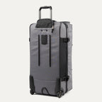 rear view of the gray black bold by travelpro large check-in drop-bottom rolling duffel bag standing vertically, showing its protective skid guards, reinforced wheel housings, two high-performance ball-bearing wheels, and extended telescoping handle.