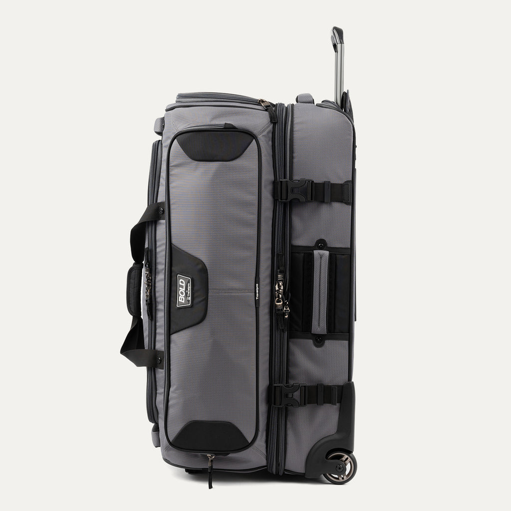 side view of the gray black bold by travelpro large check-in drop-bottom rolling duffel bag standing vertically, showing its sturdy side carry handle, exterior compression straps with buckles, and the extended telescoping handle.