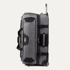 side view of the gray black bold by travelpro large check-in drop-bottom rolling duffel bag standing vertically, showing its sturdy side carry handle, exterior compression straps with buckles, and the extended telescoping handle.