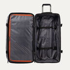 interior view of the open gray black bold by travelpro large check-in drop-bottom rolling duffel bag showing the spacious main compartment with two adjustable tie-down straps and a large zippered mesh pocket with bright orange trim on the inside lid.