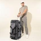 Man holding the extension handle of a Bold™ by Travelpro® Drop-Bottom Expandable Rolling Duffel in Grey/Black.
