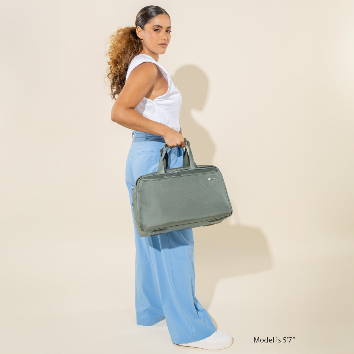 Woman Carrying the VersaPack+ UnderSeat Travel Tote with Trolley Sleeve in Green