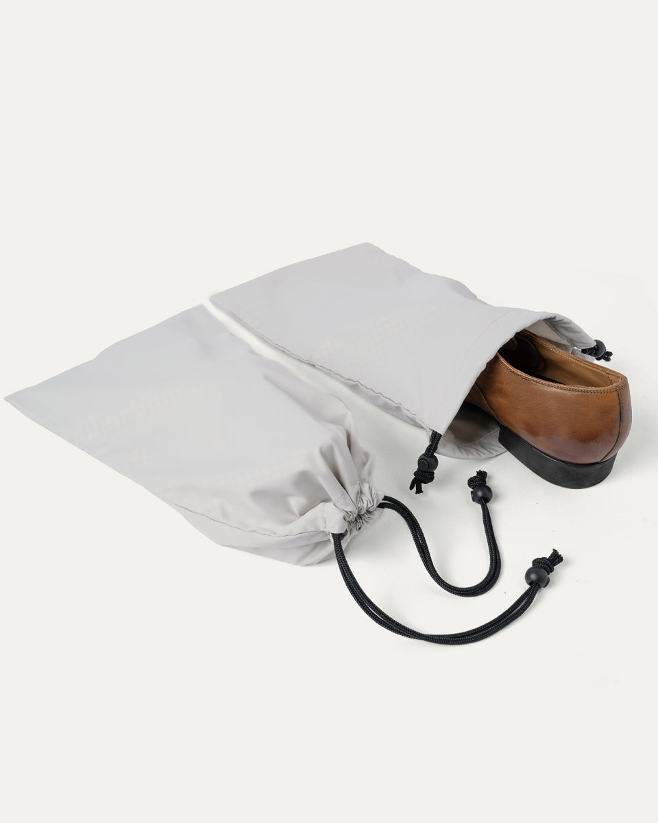 Drawstring shoe bag included with the Travelpro Platinum Reserve Compact Carry-On Hardside Spinner in Midnight Trail, shown holding a pair of shoes