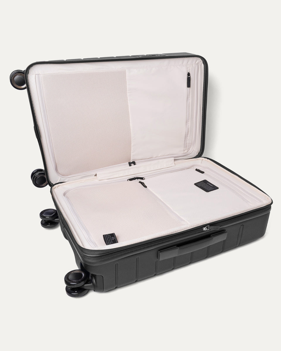 Open interior of the Travelpro Platinum Reserve Medium Check-In Hardside Spinner in Black Dust showing the zippered divider panel and dedicated pockets