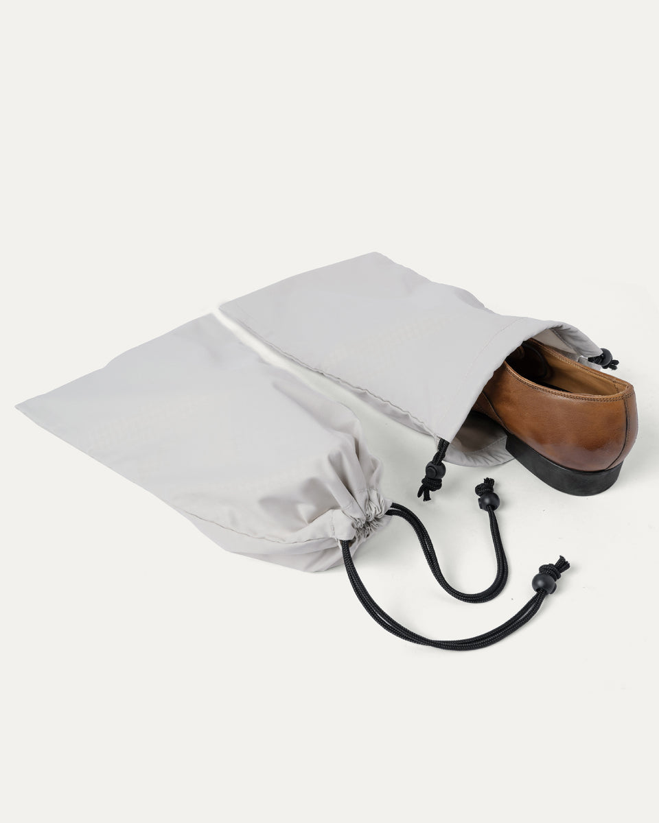 Drawstring shoe bag included with the Travelpro Platinum Reserve Large Check-In Hardside Spinner in Sandstone, shown holding a pair of shoes