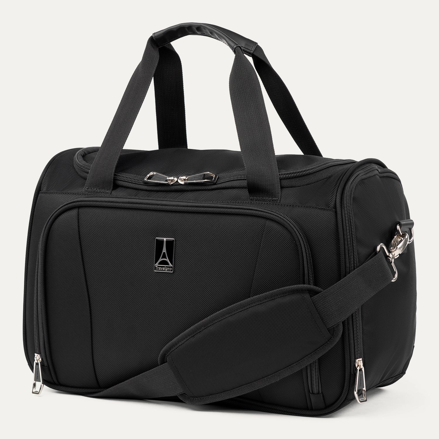 Three-quarter front view of the Travelpro Runway Tote in Black, showing dual top grab handles, an adjustable shoulder strap with a padded shoulder wrap, a front zippered compartment with the Travelpro logo badge, and silver hardware against a clean off-white background.