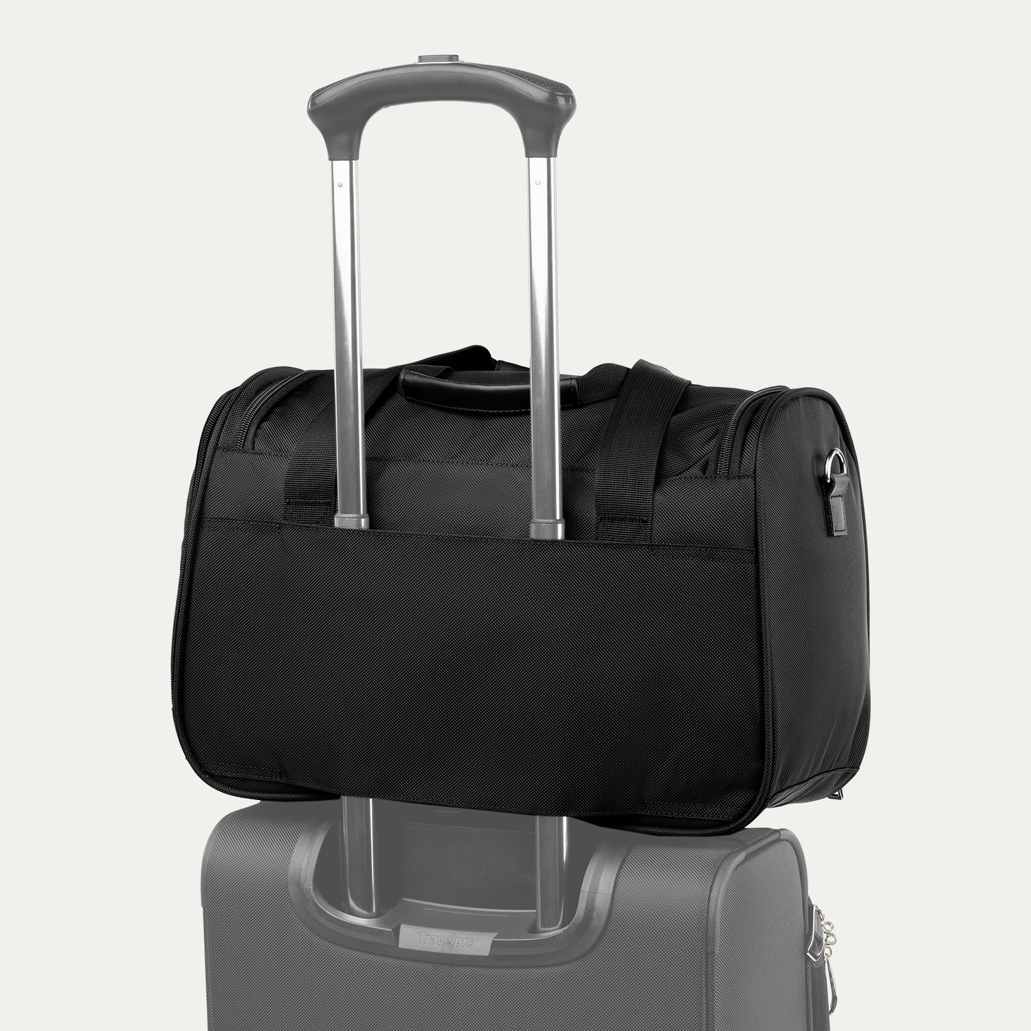 Rear view of the black Travelpro Runway Tote stacked on the telescopic handle of a matching spinner suitcase, showing the rear luggage sleeve against an off-white background.