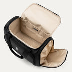 An open interior view of the black Travelpro Runway Tote, featuring a light beige lining, a zippered interior pocket with the Travelpro logo patch, and a dedicated side shoe or accessory compartment against an off-white background.