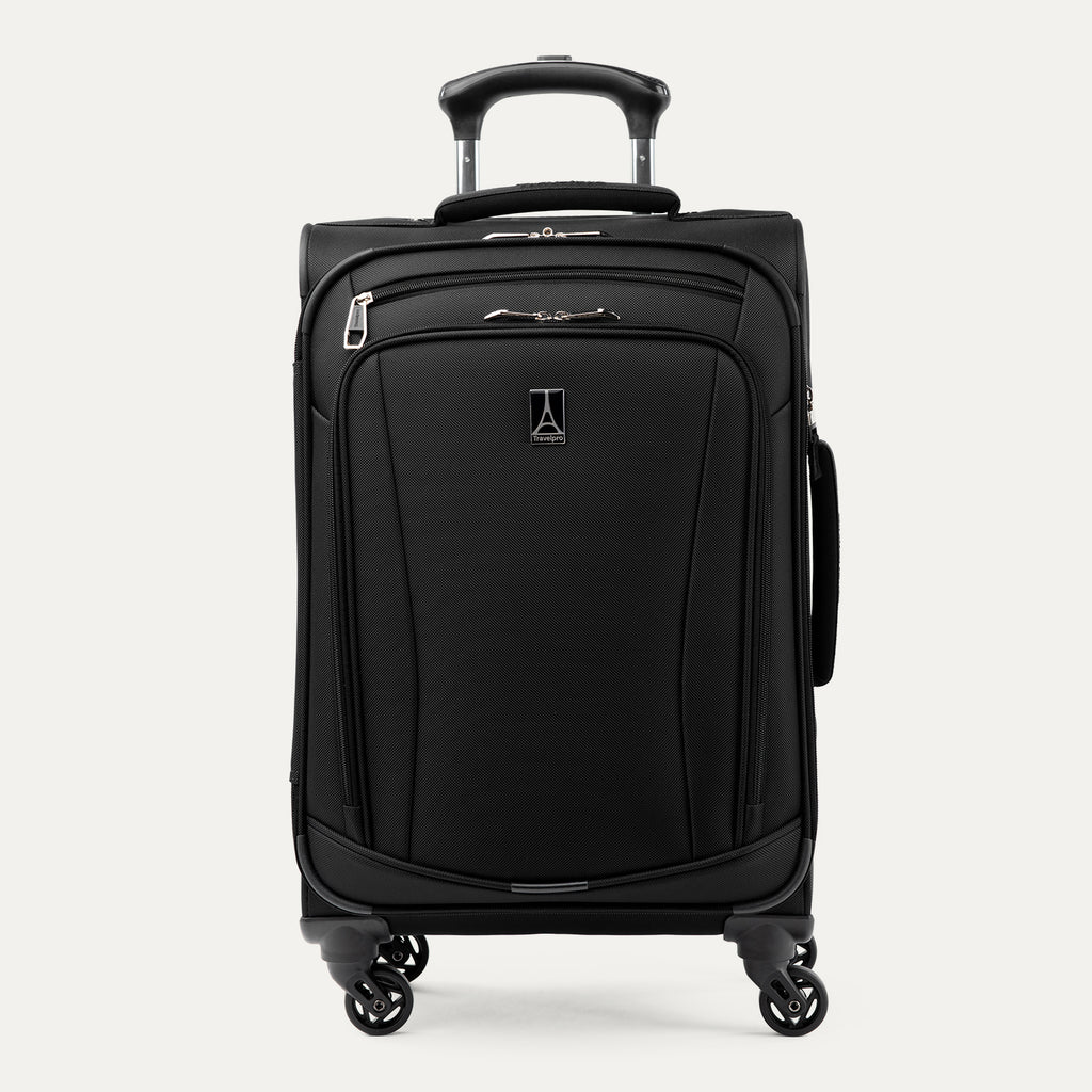 Three-quarter front view of the Travelpro Runway Tote / Carry-on Luggage Set in Black, showing the softside carry-on spinner featuring an extended telescopic handle, a zippered front pocket with the Travelpro logo badge, and multi-directional spinner wheels against a clean off-white background.