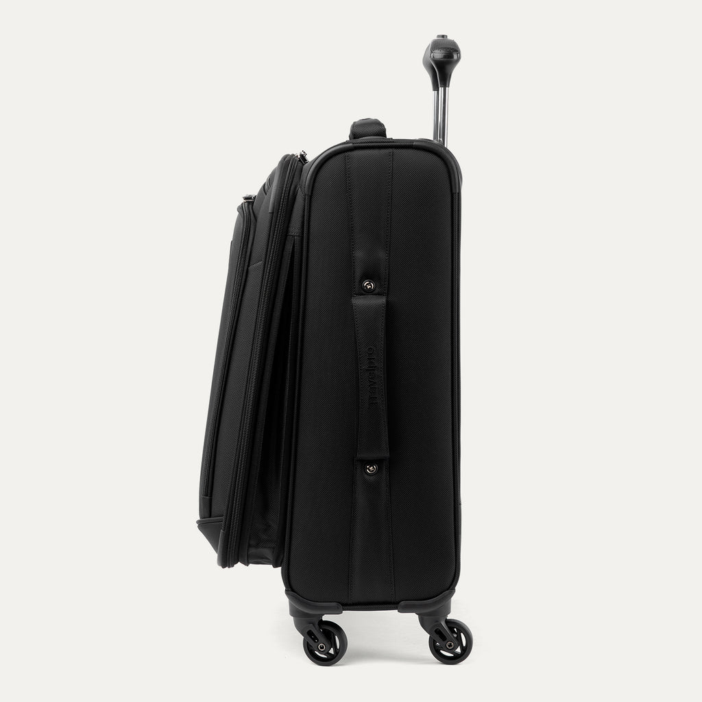 Side profile view of the Travelpro Runway Tote / Carry-on Luggage Set in Black, showing the softside carry-on spinner featuring an extended telescopic handle, a zippered front pocket with the Travelpro logo badge, and multi-directional spinner wheels against a clean off-white background.