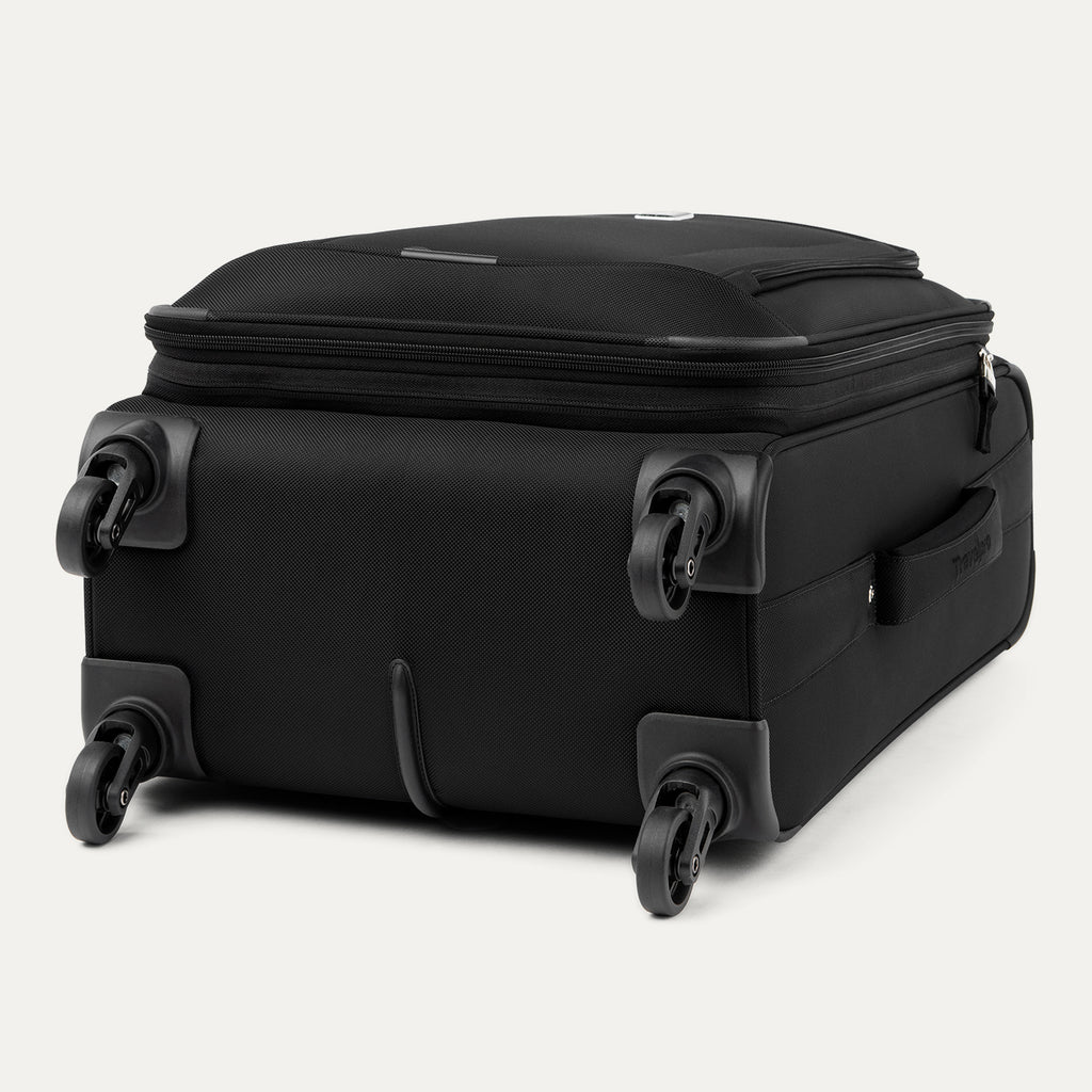 Three-quarter rear view of the Travelpro Runway Tote / Carry-on Luggage Set in Black, showing the softside carry-on spinner resting on its side wheels and corner guards against a clean off-white background.