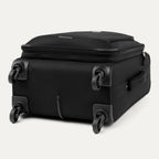Three-quarter rear view of the Travelpro Runway Tote / Carry-on Luggage Set in Black, showing the softside carry-on spinner resting on its side wheels and corner guards against a clean off-white background.