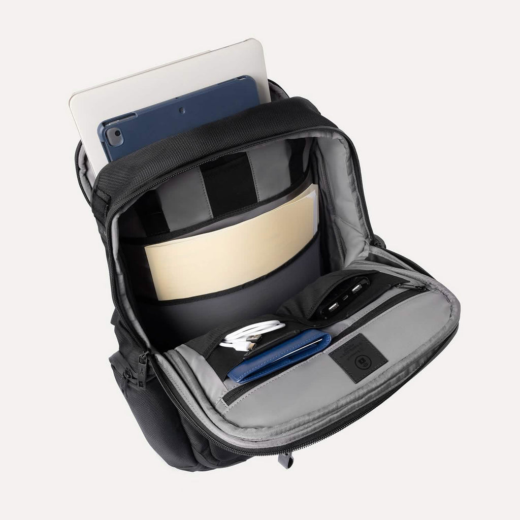 Black backpack with compartments containing a tablet, notebook, and other items on a white background