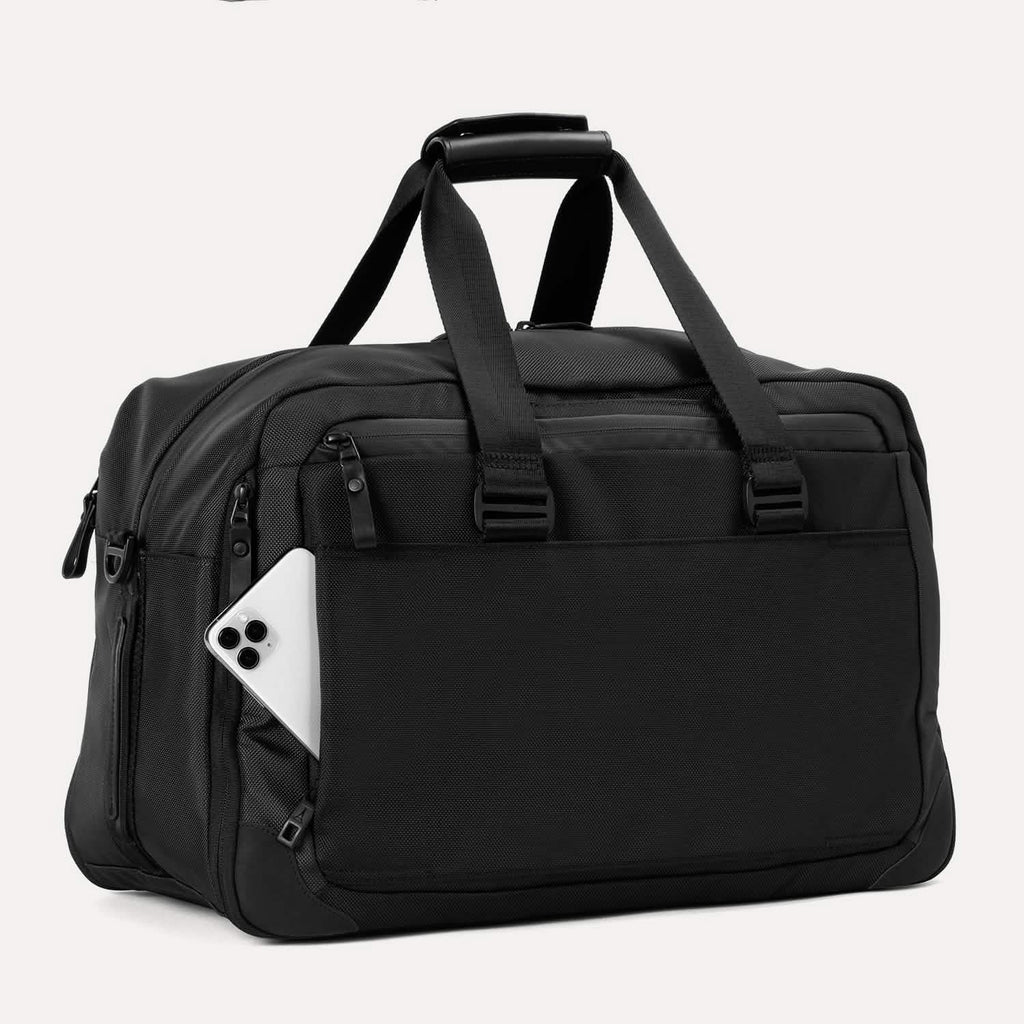 Slanted rear view of Travelpro Altitude Double Expansion Duffel in Jet Black with phone in QuickSlip Pocket, top handle, and dual straps.

