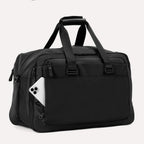 Slanted rear view of Travelpro Altitude Double Expansion Duffel in Jet Black with phone in QuickSlip Pocket, top handle, and dual straps.
