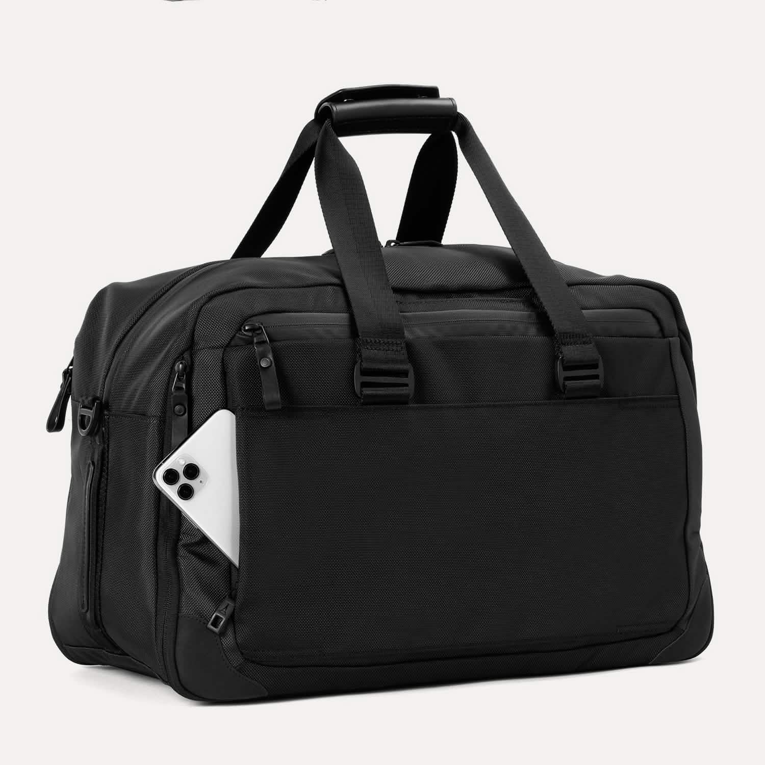 Slanted rear view of Travelpro Altitude Double Expansion Duffel in Jet Black with phone in QuickSlip Pocket, top handle, and dual straps.

