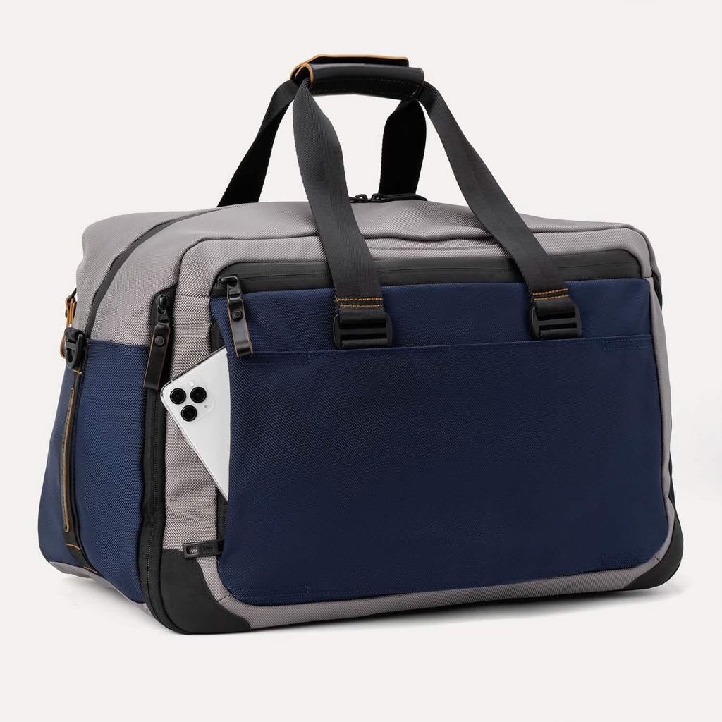 Slanted rear view of the Travelpro® Altitude™ Double Expansion Duffel in Stellar Navy/Grey, featuring dual carry handles with reinforced stitching and a exterior slip pocket holding a smartphone.
