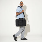 Model carrying the Travelpro® Altitude™ Full Expansion Brief in Black over the shoulder using the adjustable padded strap, showcasing its sleek front design with dual top handles
