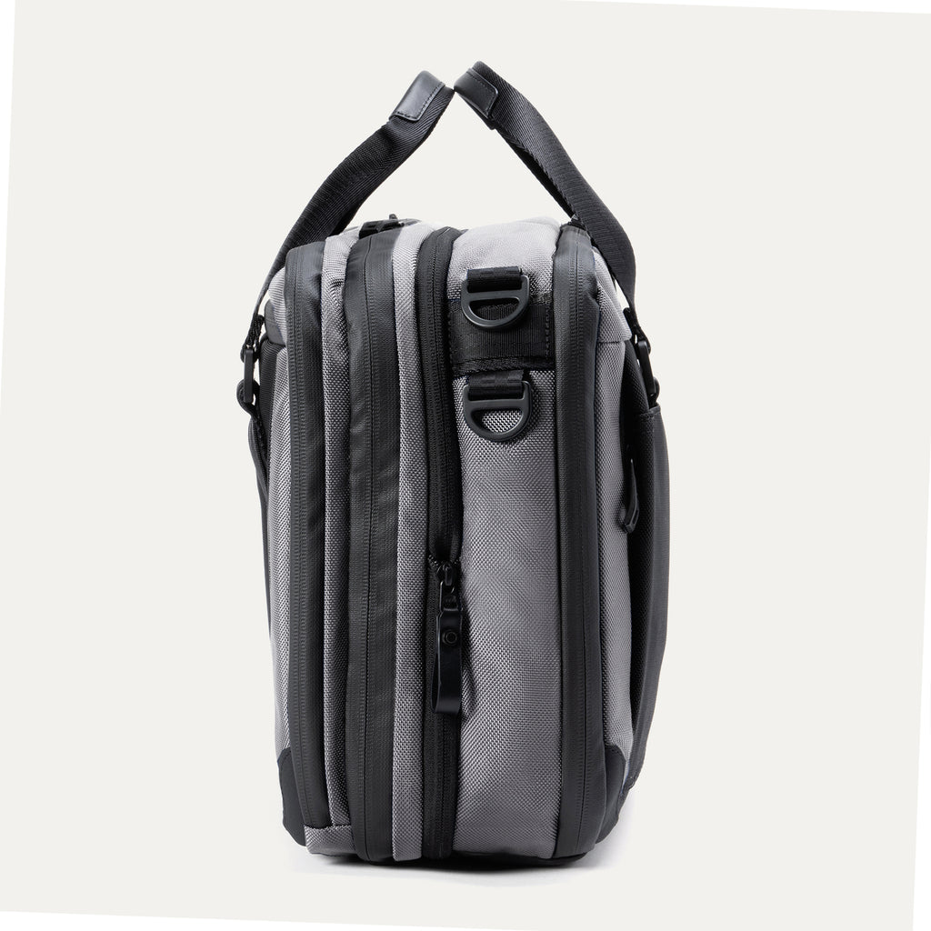 Side view of the Travelpro® Altitude™ Full Expansion Brief in Falcon Grey showing its compartments, zippers, and attachment points for a shoulder strap.
