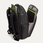 Three‑quarter rear view of the Travelpro Altitude Large Backpack in Neon Shadow, showing black textured exterior with neon yellow accents, open main compartment with gray lining, and multiple zippered pockets against a light background.