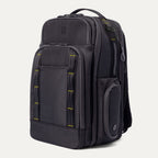 Three‑quarter front view of the Travelpro Altitude Large Backpack in Neon Shadow, showing black textured exterior with neon yellow stitching accents, multiple zippered compartments, and an iPhone in the front pocket against a light background.