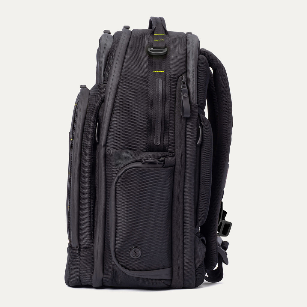 Side profile view of the Travelpro Altitude Large Backpack in Neon Shadow, showing black textured exterior with neon yellow accent panel, multiple zippered pockets, and padded shoulder straps against a light background.