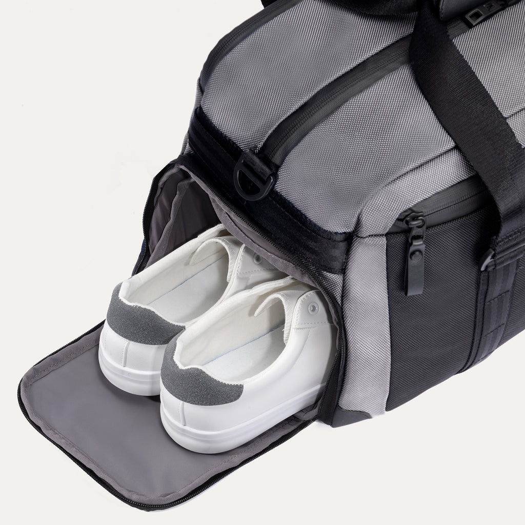  Travelpro Altitude Day-to-Day Duffel in Falcon Grey, with shoe compartment open and sneakers neatly stowed inside.

